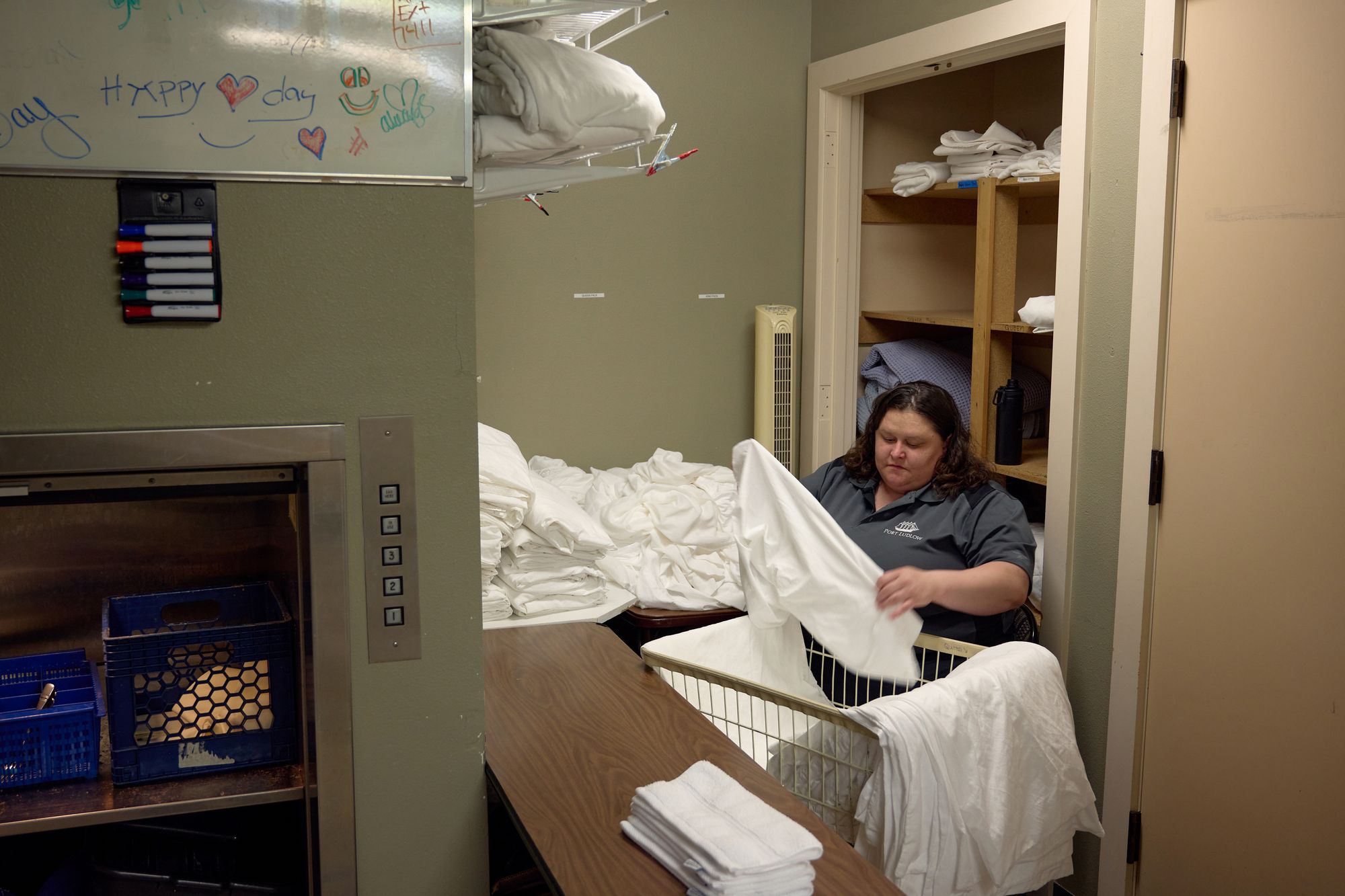 A White woman with medium-length wavy brown hair folds sheets in a laundry room . 