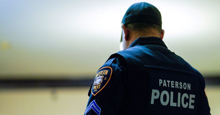 A photo shows the back of a police officer, with the words "Paterson Police" on their uniform.