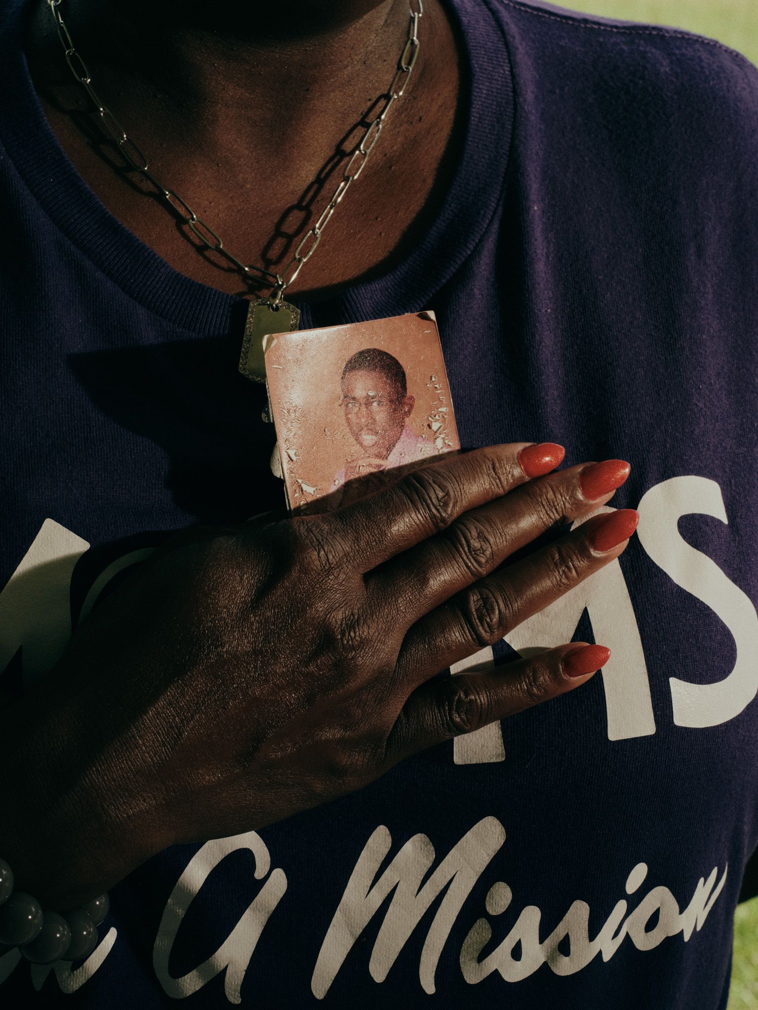 Lennie Ross, a Black woman, holds a small photo of a young Black man close to her chest. She is wearing a purple T-shirt that says “Moms on a Mission.”