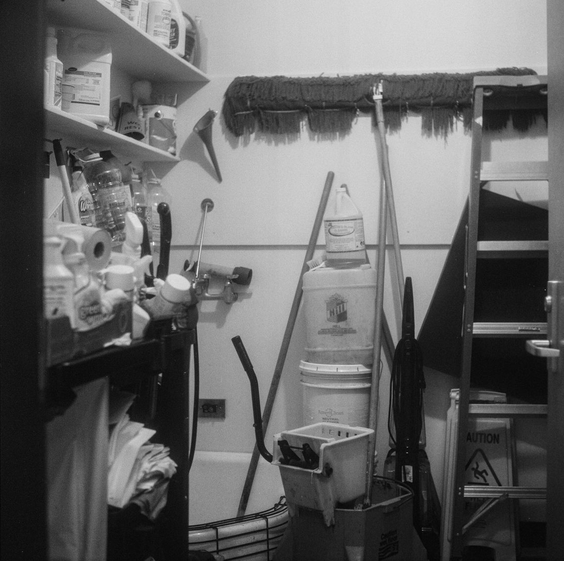 A black-and-white photo of a janitor’s closet filled with cleaning supplies. 