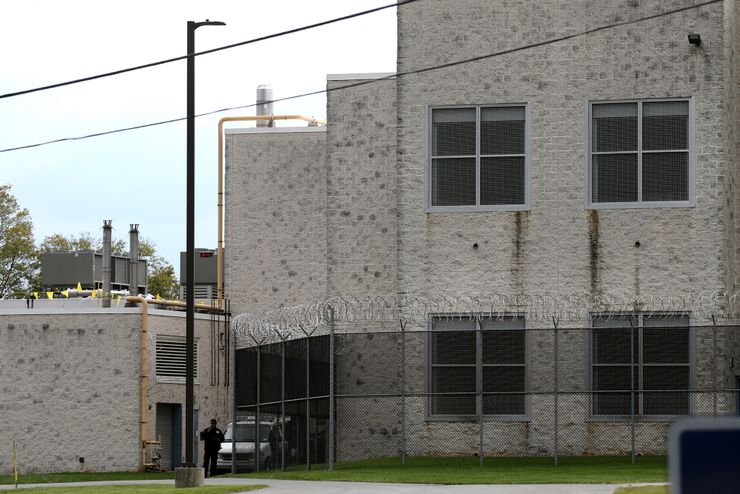 A photo shows a gray brick prison building surrounded by barbed wire fencing. 