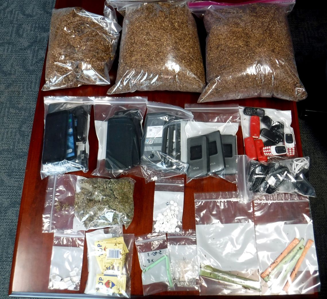 A photo shows a brown table and on it, from top to bottom: three bags with a brown substance in it, bags of cell phones, a bag of white pills, a bag with square, thin objects in it; and three bags with multi-colored tubes. 