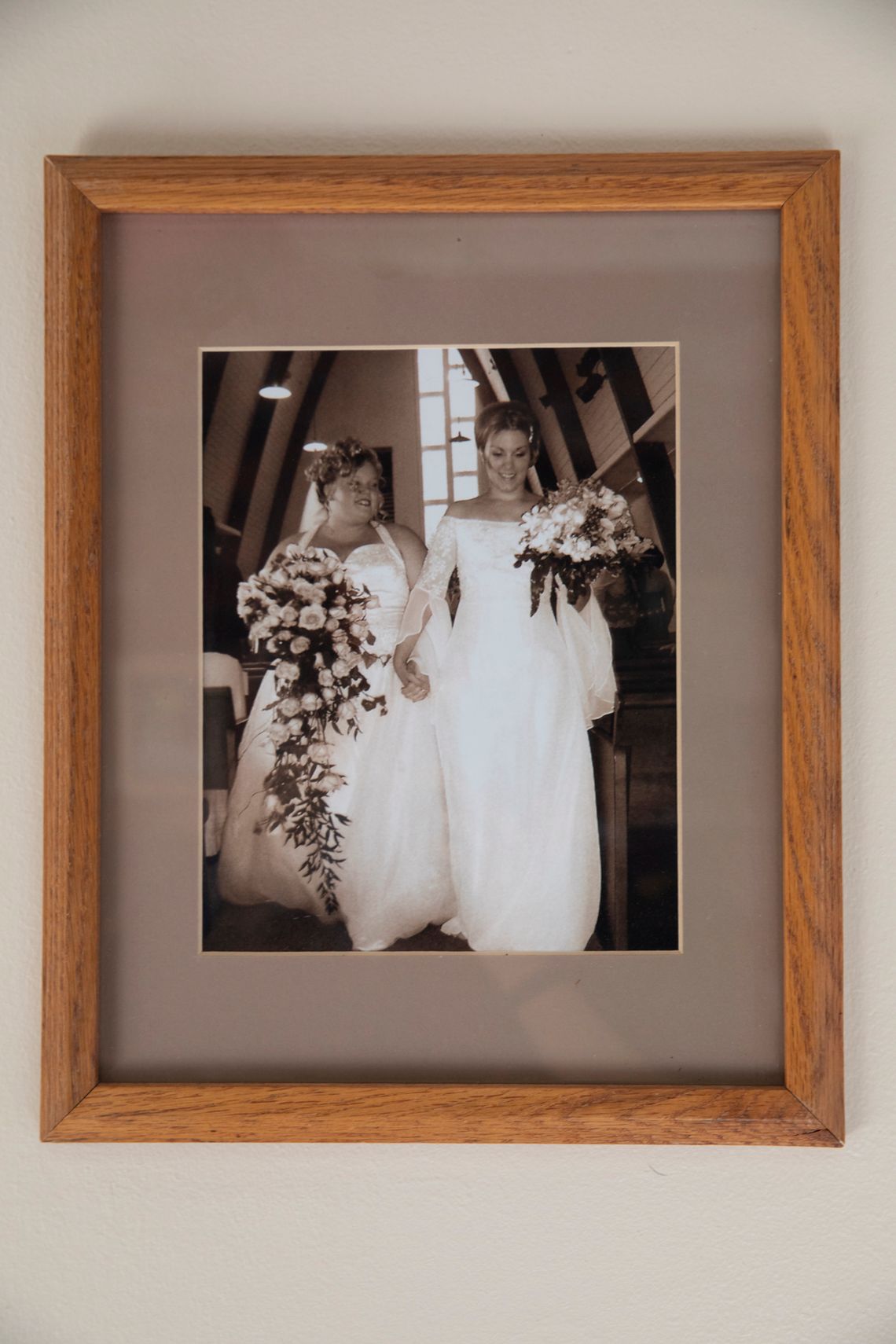 Jules and Samantha Werkheiser, both White women, on their wedding day in white dresses and holding flowers. 