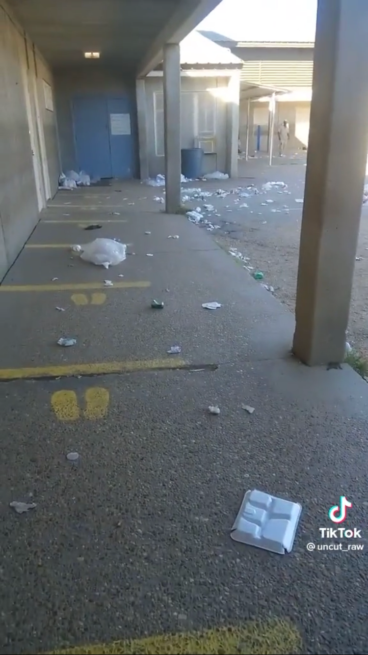 Trash spread out in an outdoor hallway of a prison facility.