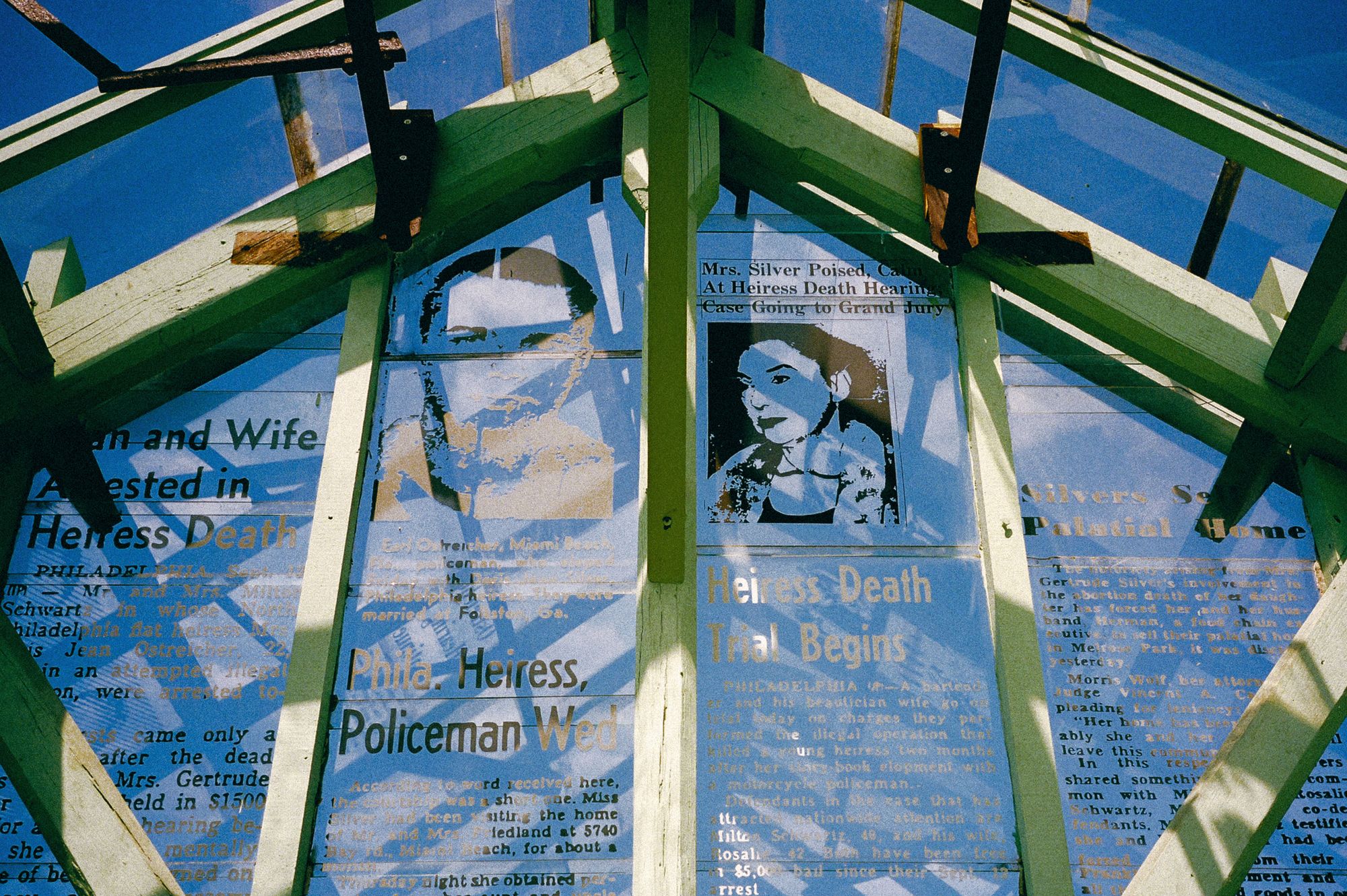 Newspaper clippings showing photos and text about Doris Jean Ostreicher are printed on the glass walls of a greenhouse. 