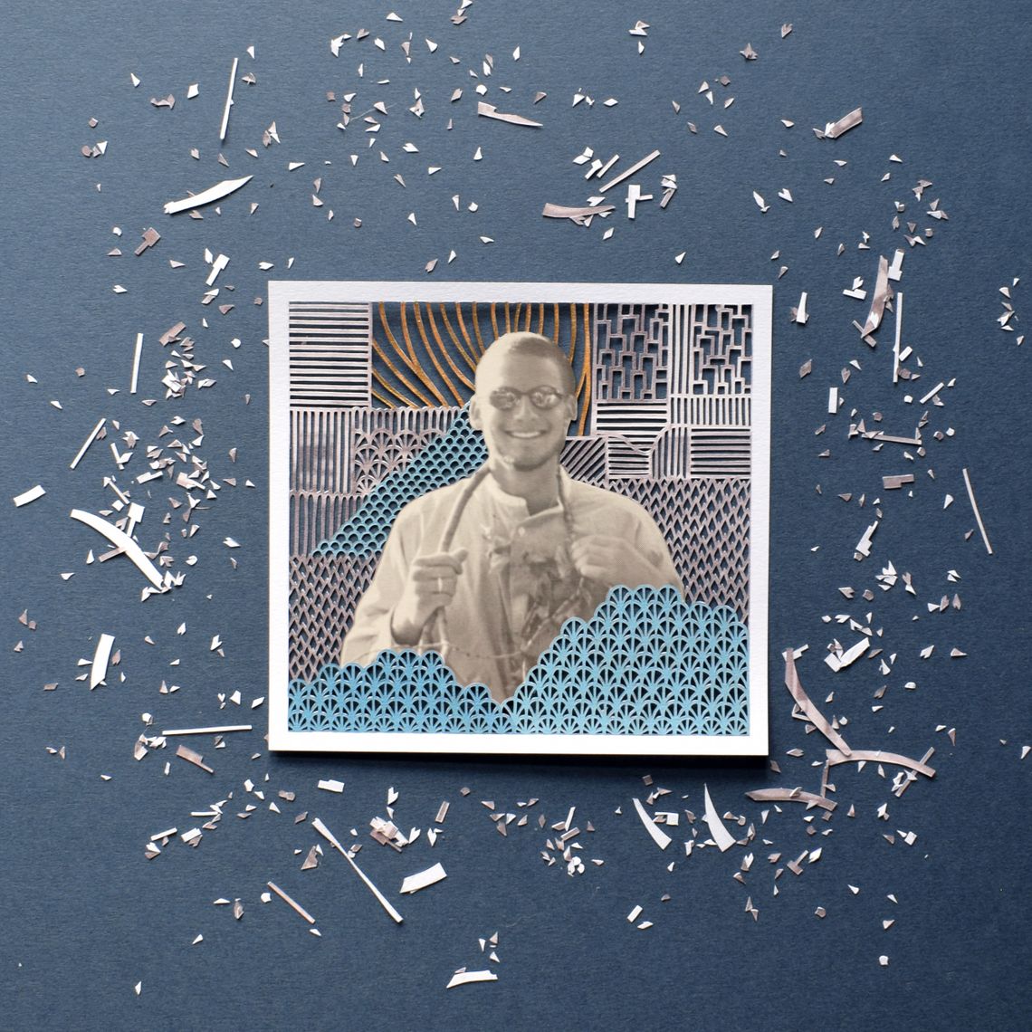 A yearbook photo of Leon Jacob, a White teen boy, is situated in the center of a paper cut illustration, with small designs cut out of the background. Tiny pieces of paper are scattered around the photo. 