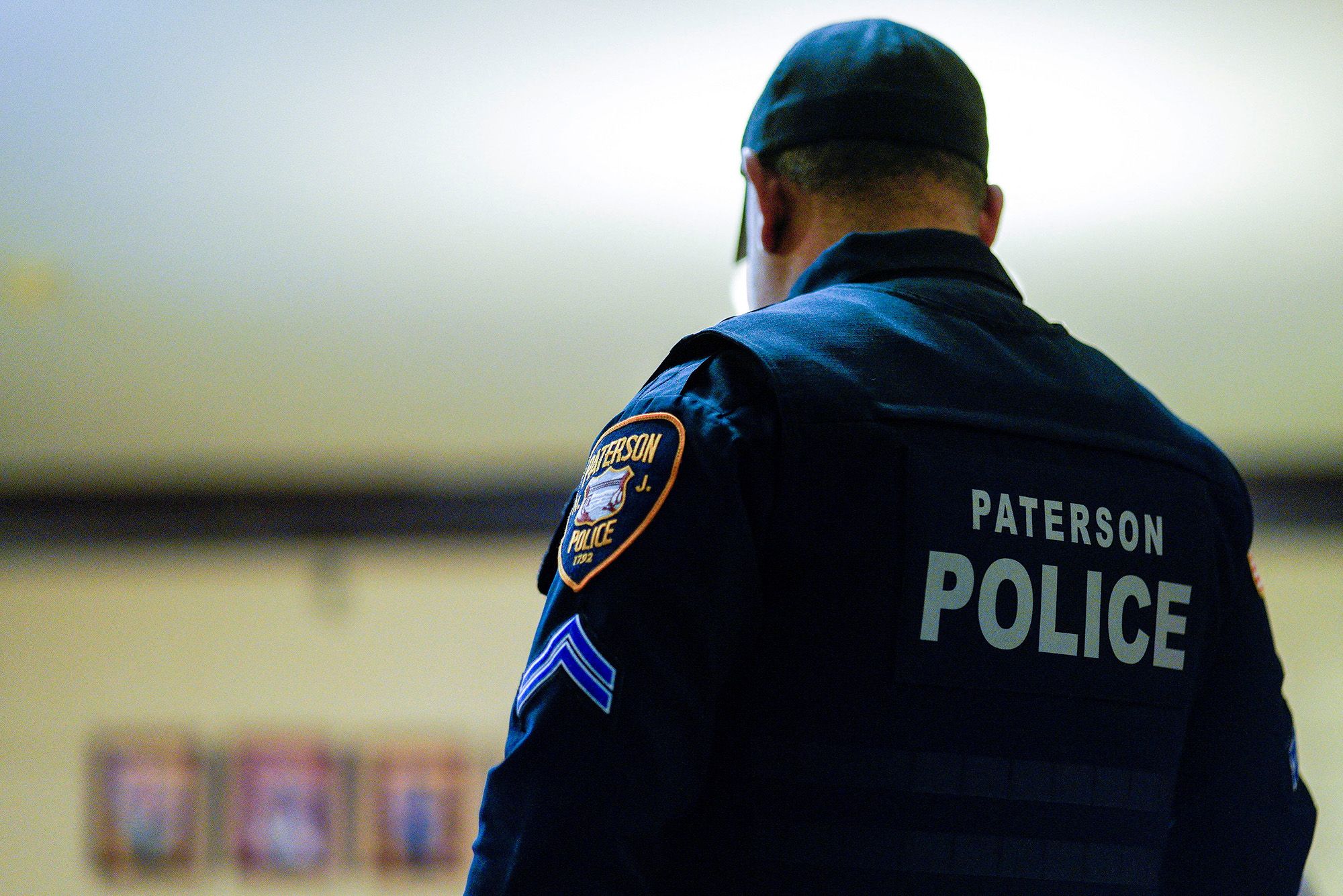 A photo shows the back of a police officer, with the words "Paterson Police" on their uniform.