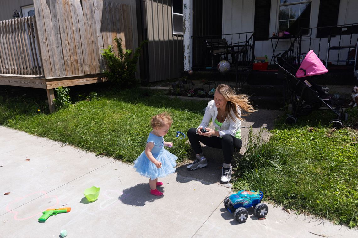 A photo of a White woman sitting outside and playing with a remote-controlled car with her daughter.