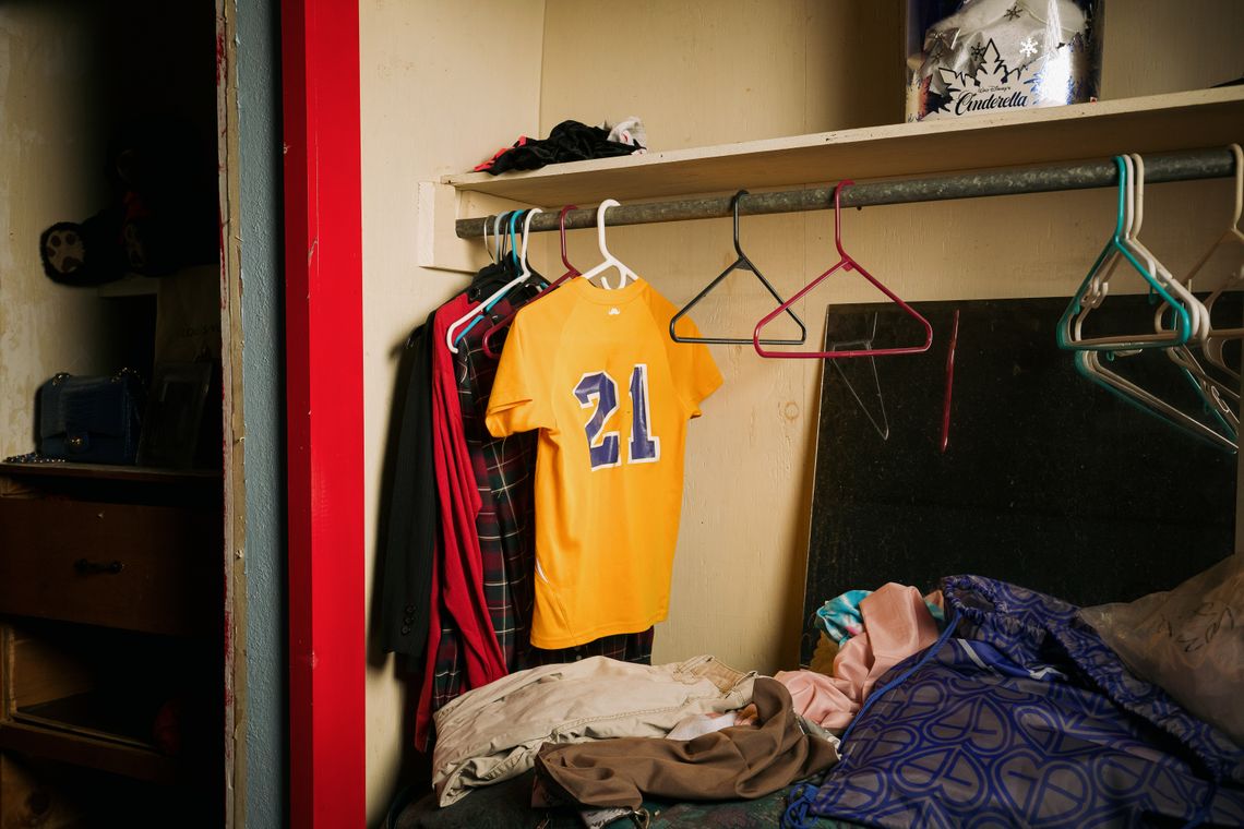 A marigold-colored baseball jersey hangs in a closet with a few other shirts. 