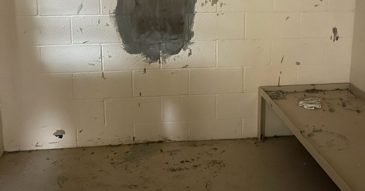 The wall of a cell shows an area with gray exposed paint in the shape of a hole.  