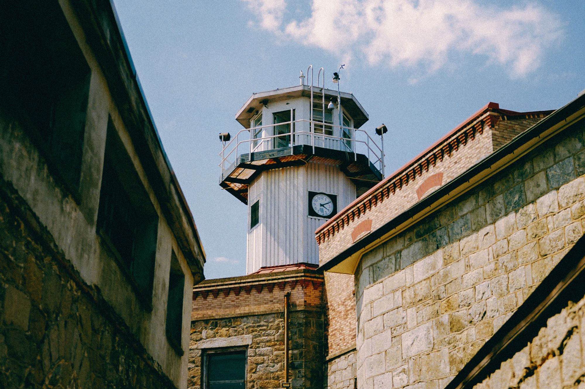 A white guard tower has a clock on the side, and stone buildings that are part of the prison are visible in the foreground. 