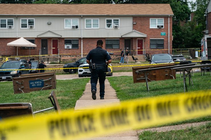A photo shows a police officer walking through a crime scene investigation surrounded by police tape in a residential area. 