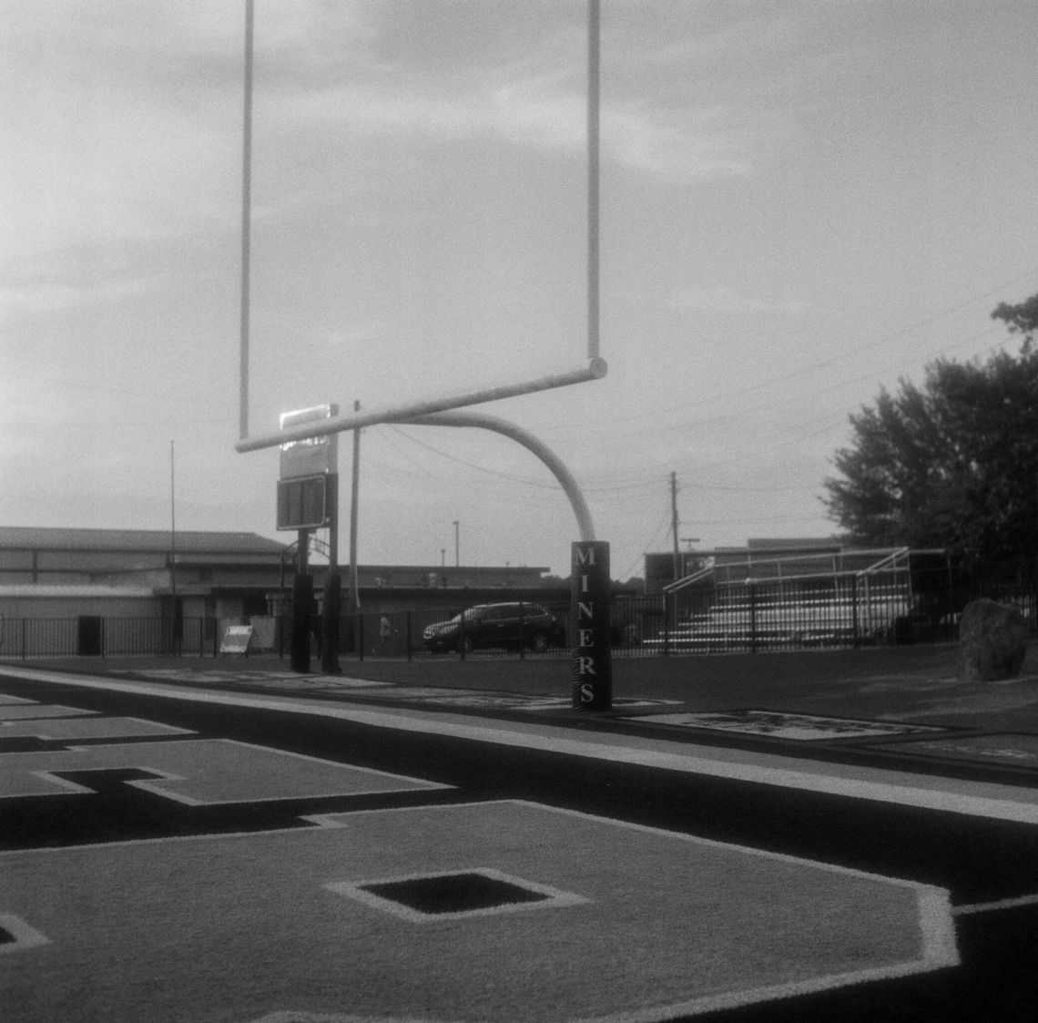 Three black-and-white photos show different views of a padded goalpost on a football field. 