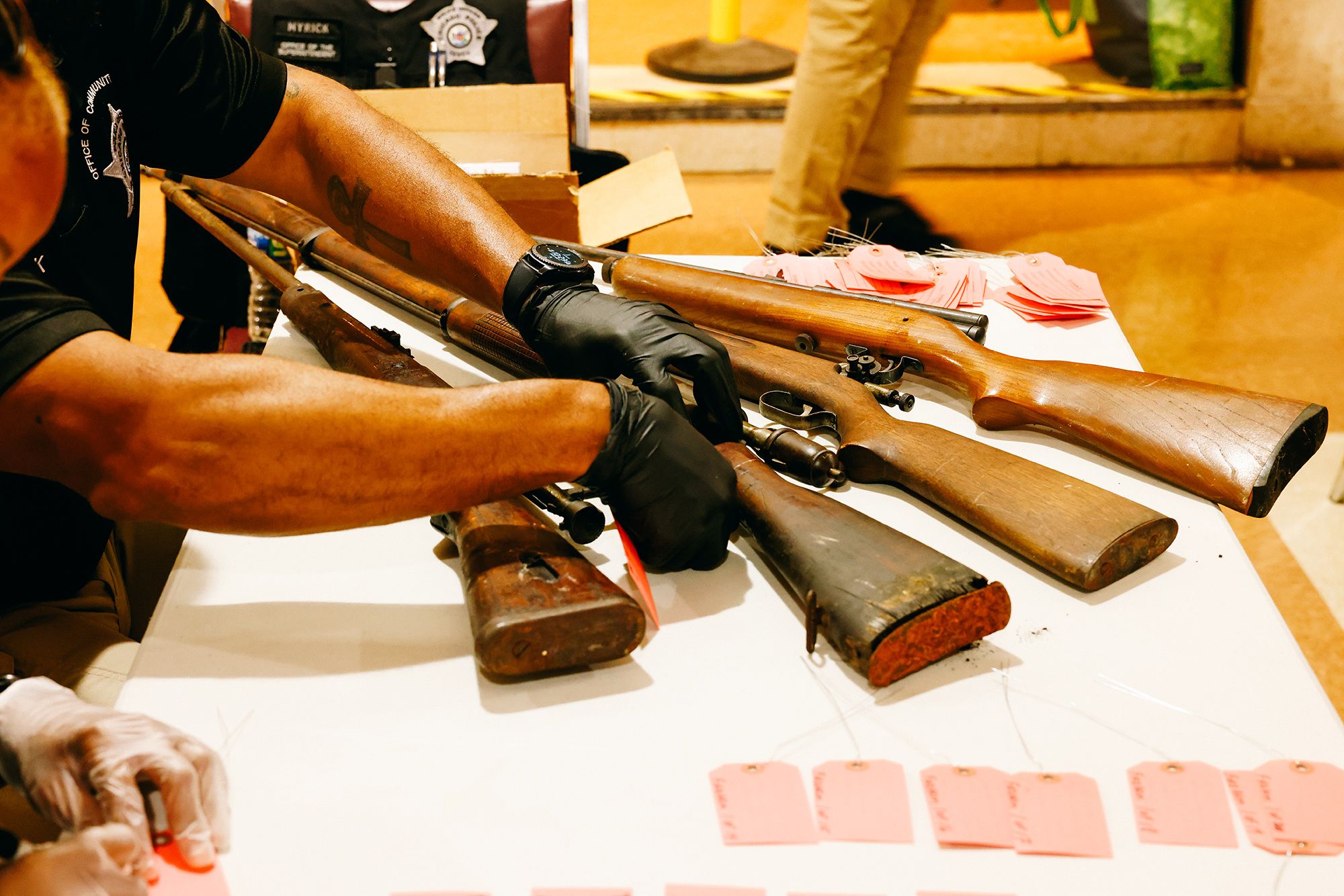 An officer inspects one of the four long guns on a table. 