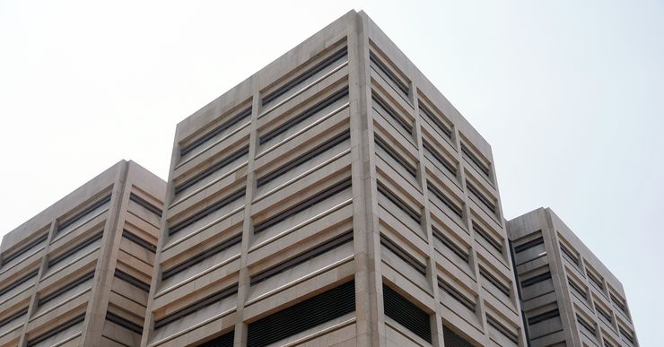 A photo, taken from a low angle, shows the outside of a light brown tower with narrow, horizontal windows. The sky is visible above the building.