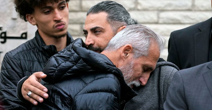 A elderly Palestinian man, wearing a black puffer jacket, hugs another Palestinian man.