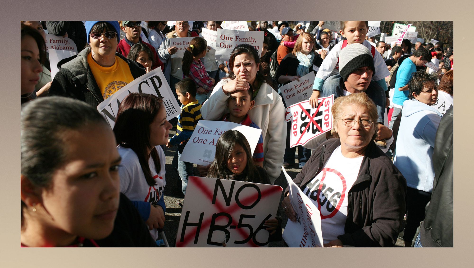 A photo shows a crowd of mostly Latino people of different ages holding signs and wearing shirts against HB-56. 