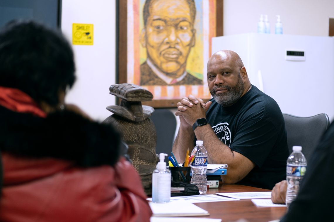 Fred Ward, in a black T-shirt, sits at a table with other people. 