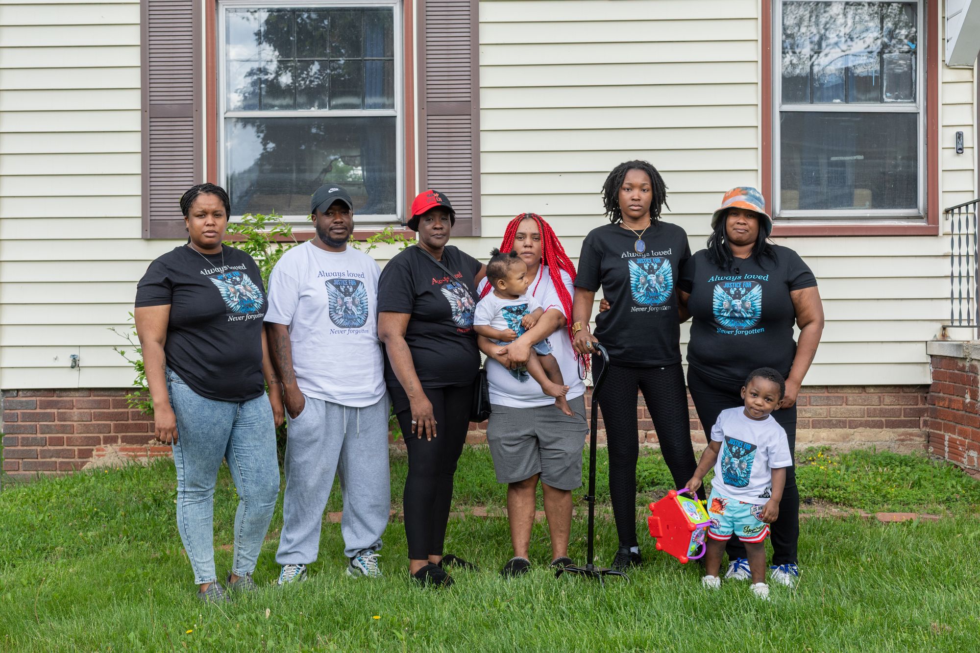 A photo of a Black family of different ages posing for a portrait. Each family member is wearing a black or white shirt with blue text that reads “Always Loved: Justice for Nathan Kinney.” 