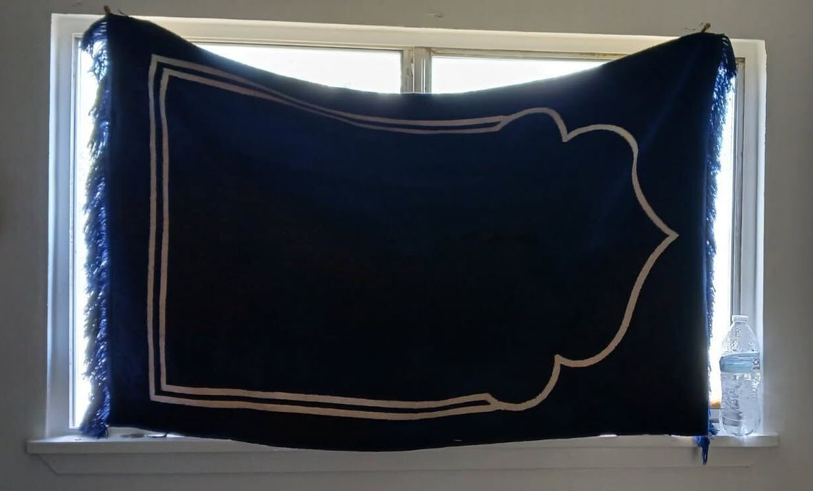A photo shows a blue-and-white prayer rug covering a window.
