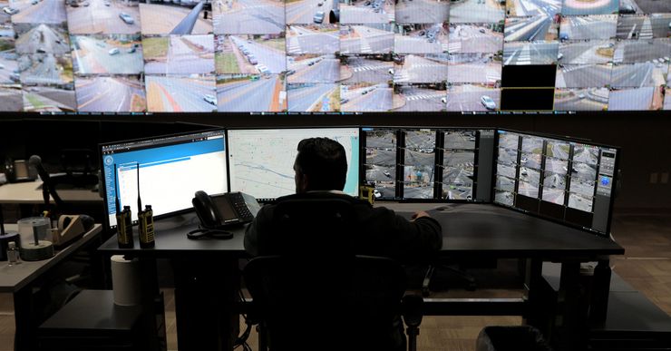 A detective sits in a CCTV control room, reviewing multiple videos captured by different surveillance cameras. 