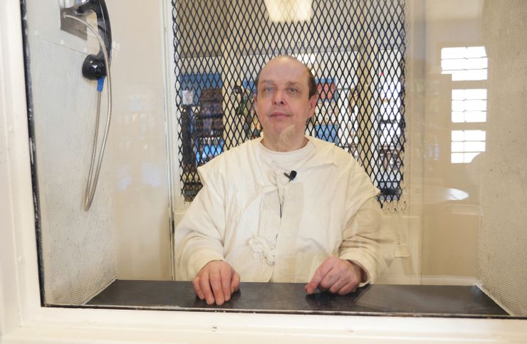 Robert Roberson, a White man wearing a prison uniform, sits in a phone booth behind glass at the Allan B. Polunsky Unit. 