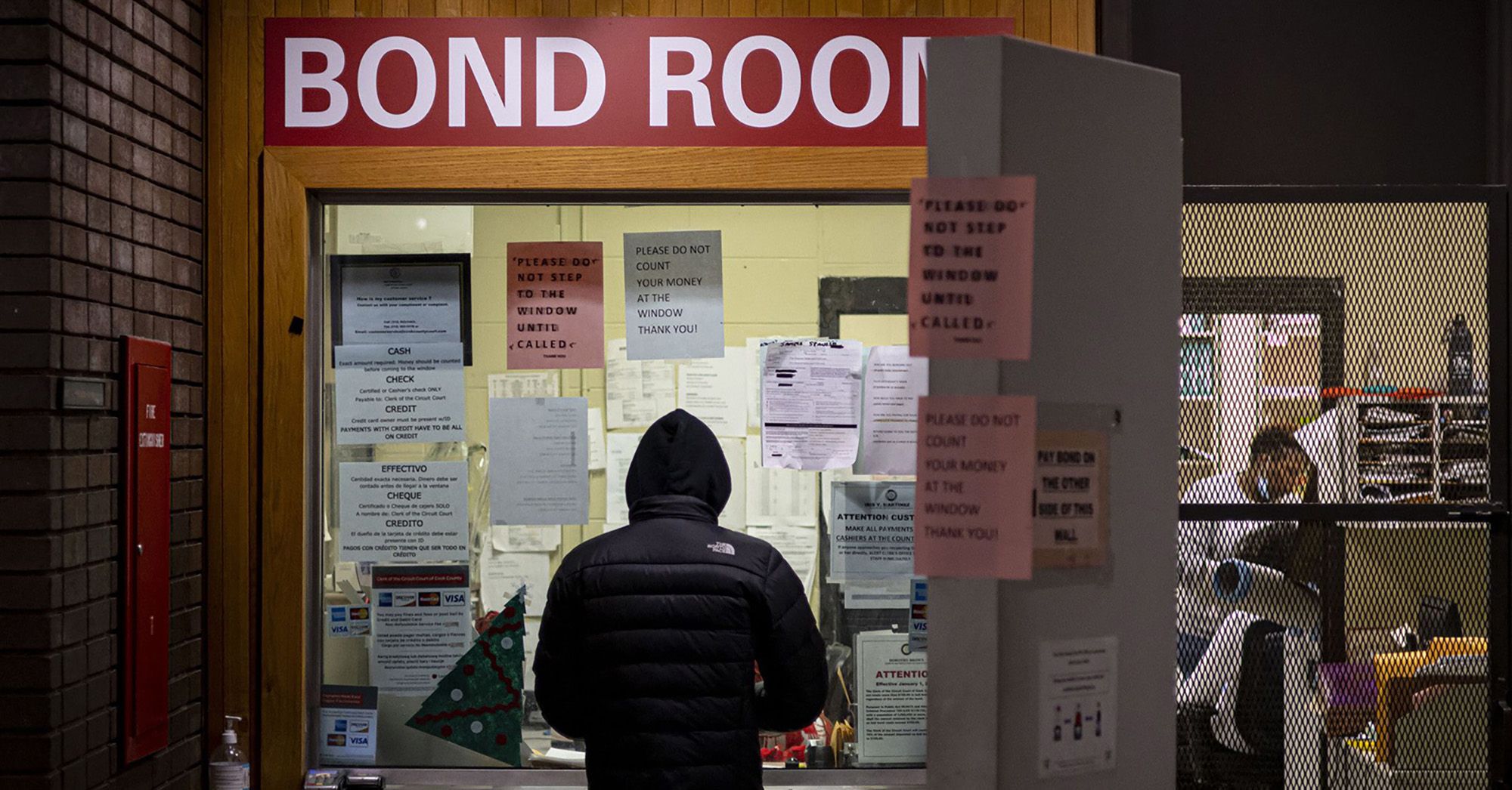 A person in a black jacket stands at the window of a bail bonds office. 
