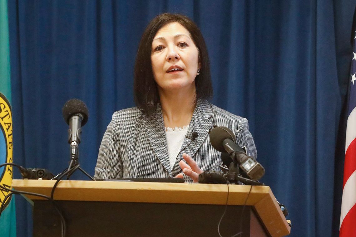 A female prosecutor, wearing a gray suit, speaks at a podium. 