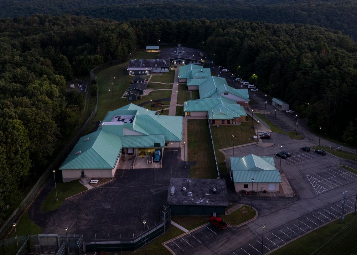 An aerial photo shows the campus of a residential treatment facility with a light green roof during sunset. The facility is surrounded by a forest and hills.