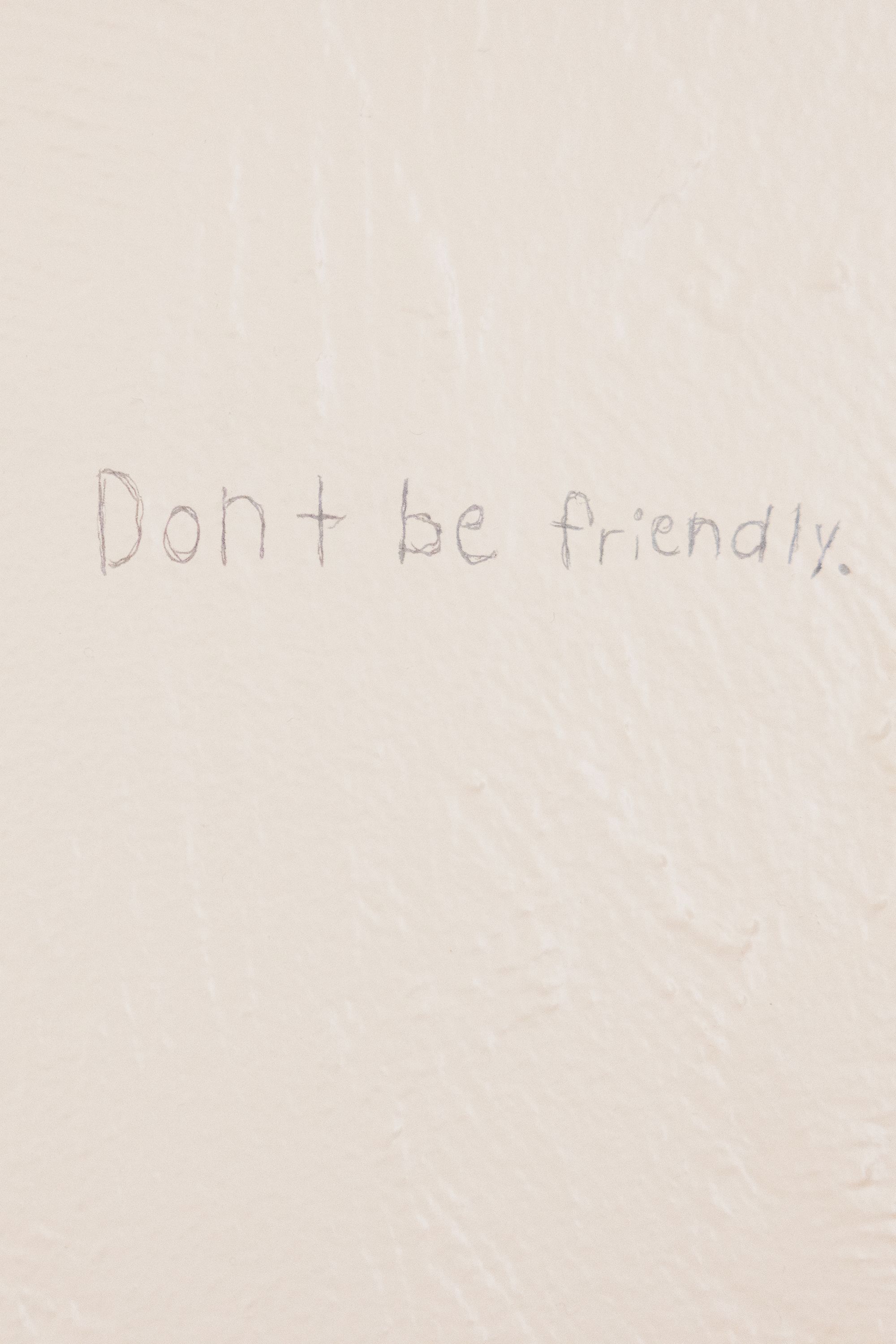 Handwriting on an off-white wall reads "Don't be friendly." 
