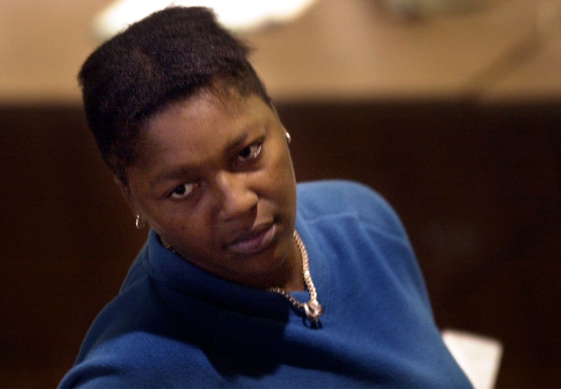 A Black woman in a blue sweatshirt sits in a courtroom. 