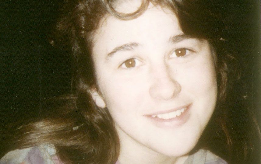 A young White woman with curly, dark brown hair, smiling toward the camera.