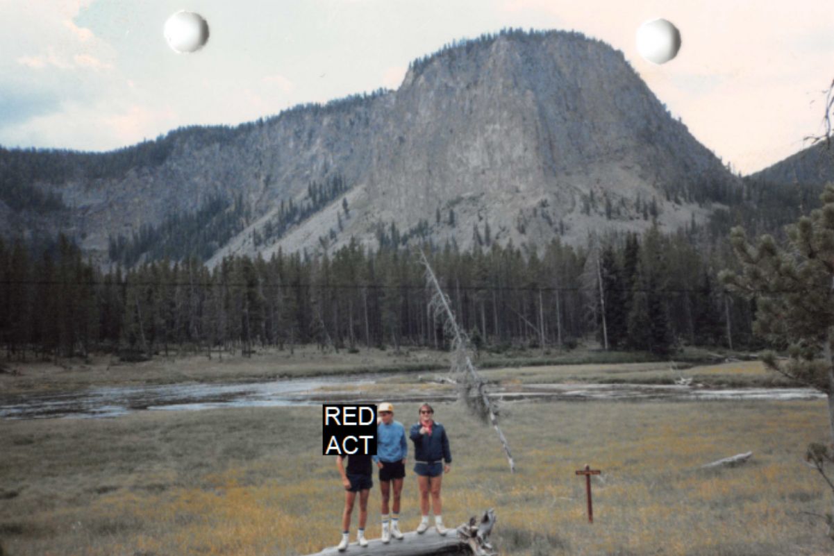 Jake, a multiracial teenage boy, stands next to Bill Hammond, a White man, in front of a mountain range. 